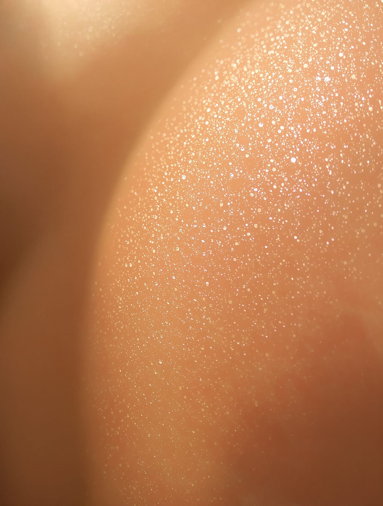 Luminous skin macro showing natural texture and golden light on the shoulder